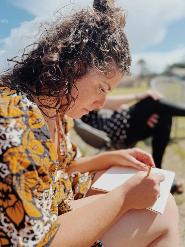 Virginia outdoors in a patterned shirt, head down, drawing in a sketchbook