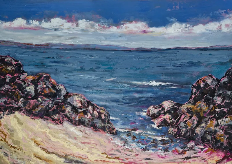 A pale sandy cove between dark rocks opening onto deep blue sea, low hills across the water under a band of white cloud
