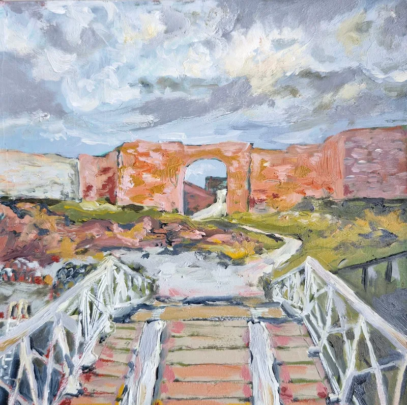 White railings of a footbridge leading towards a red sandstone arch at Dunbar harbour, under a grey and white sky