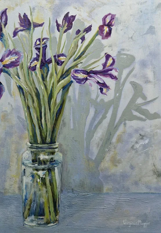 Purple irises in a clear glass jar of water against a pale grey wall, their shadows falling behind them