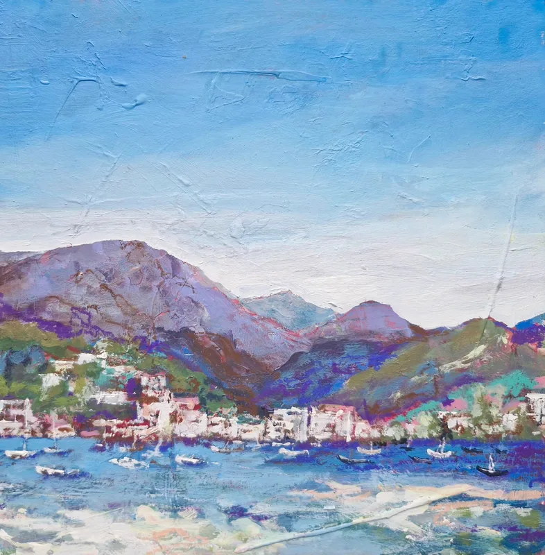 Purple mountains rising behind a white harbour town, small boats on bright blue water in the foreground