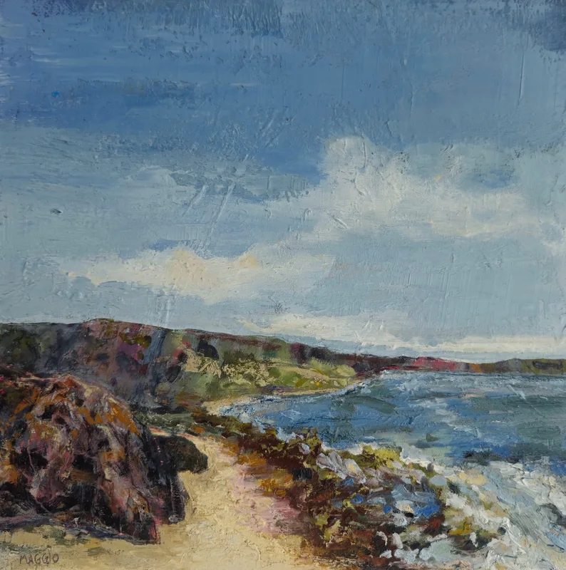 A sandy path along a grassy headland above blue sea, a dark rock in the foreground and white clouds overhead