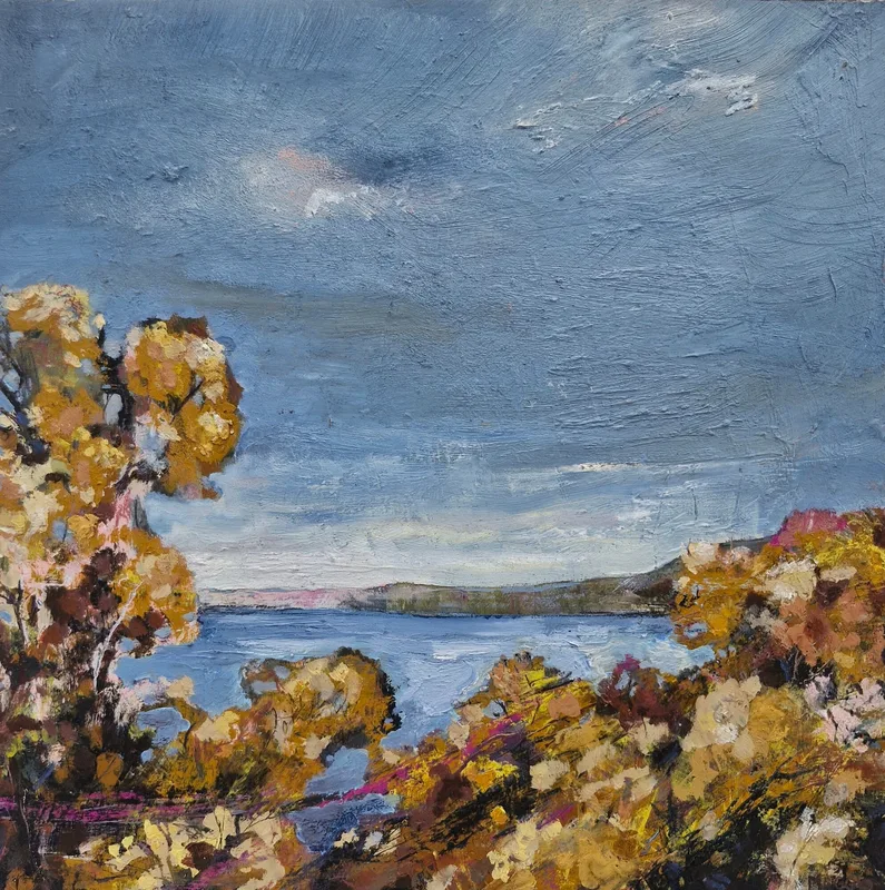 Golden gorse bushes framing a view down to calm blue water and a distant headland under a grey blue sky