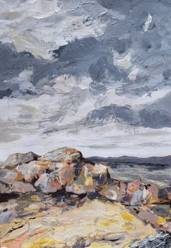 Piled pink and grey rocks on a sandy shore, the sea and a grey sky beyond